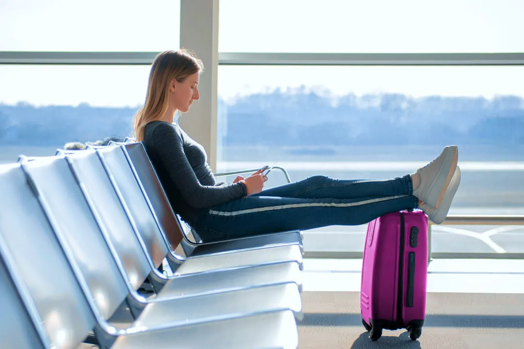 Девушка положила ноги на фиолетовый чемодан