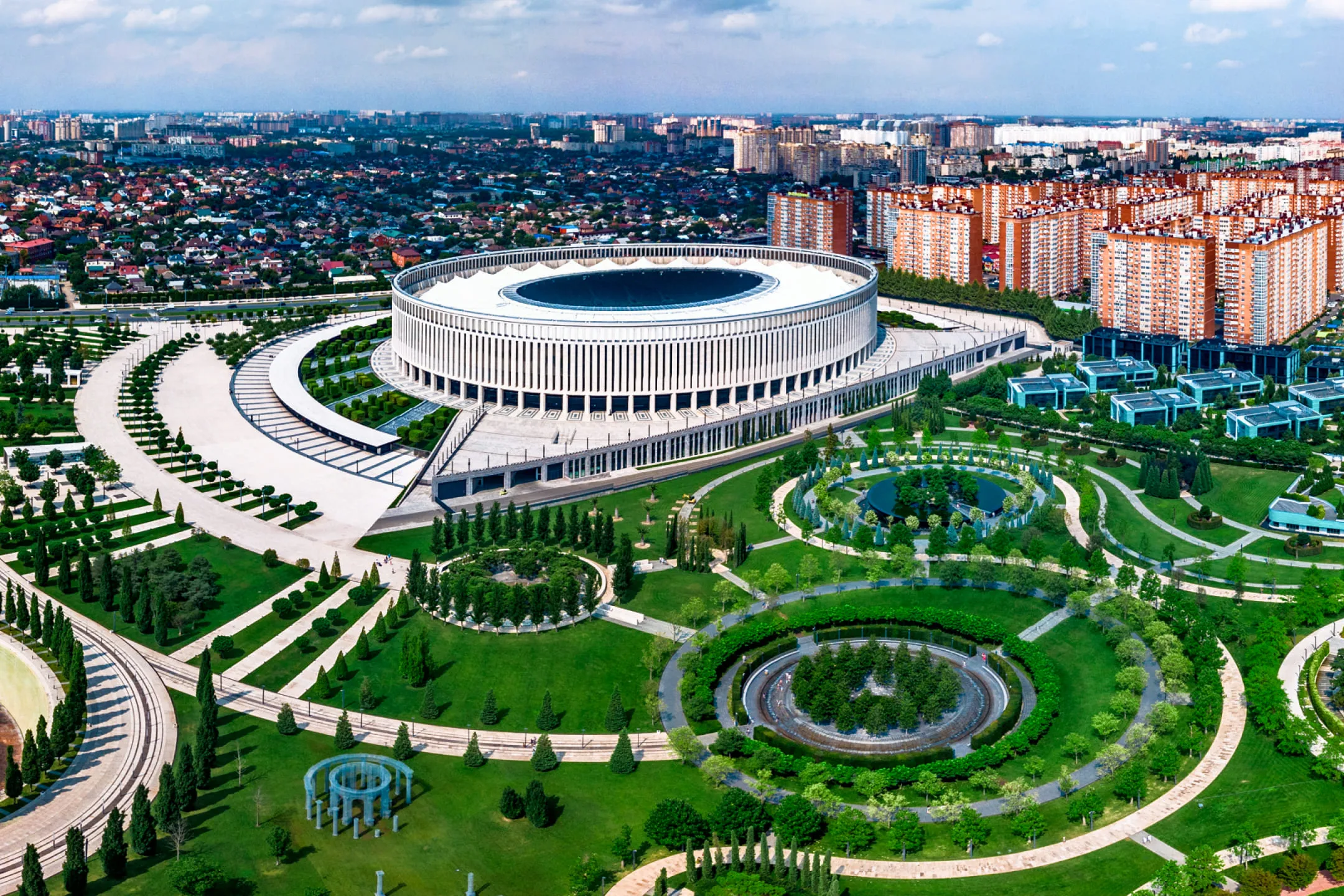 Белое здание в центре парка с круговыми дорожками и подстриженными деревьями