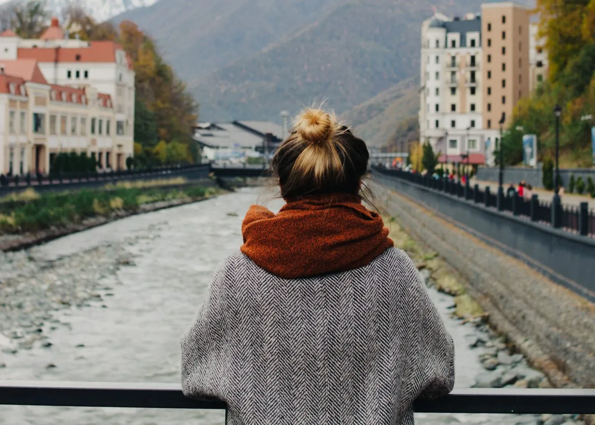 Девушка облокотилась на перила и смотрит на реку