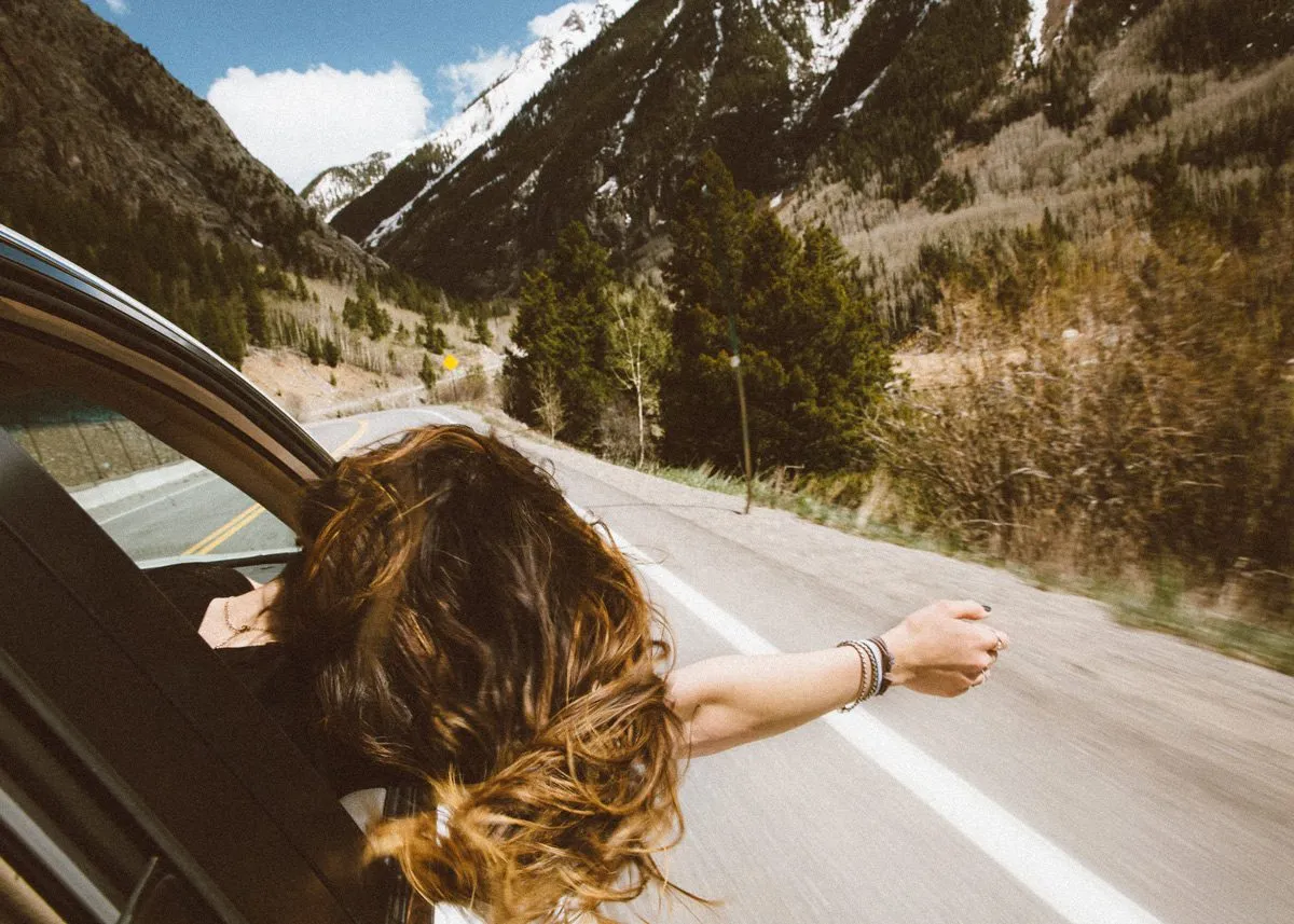 Девушка высовывает голову из окна автомобильной машины