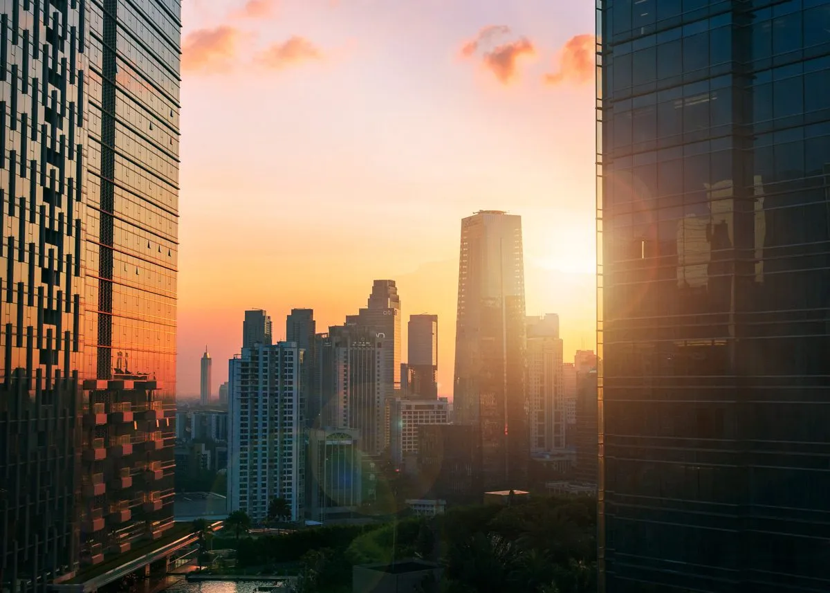 Проглядывающие между многоэтажными зданиями лучи закатного слонца